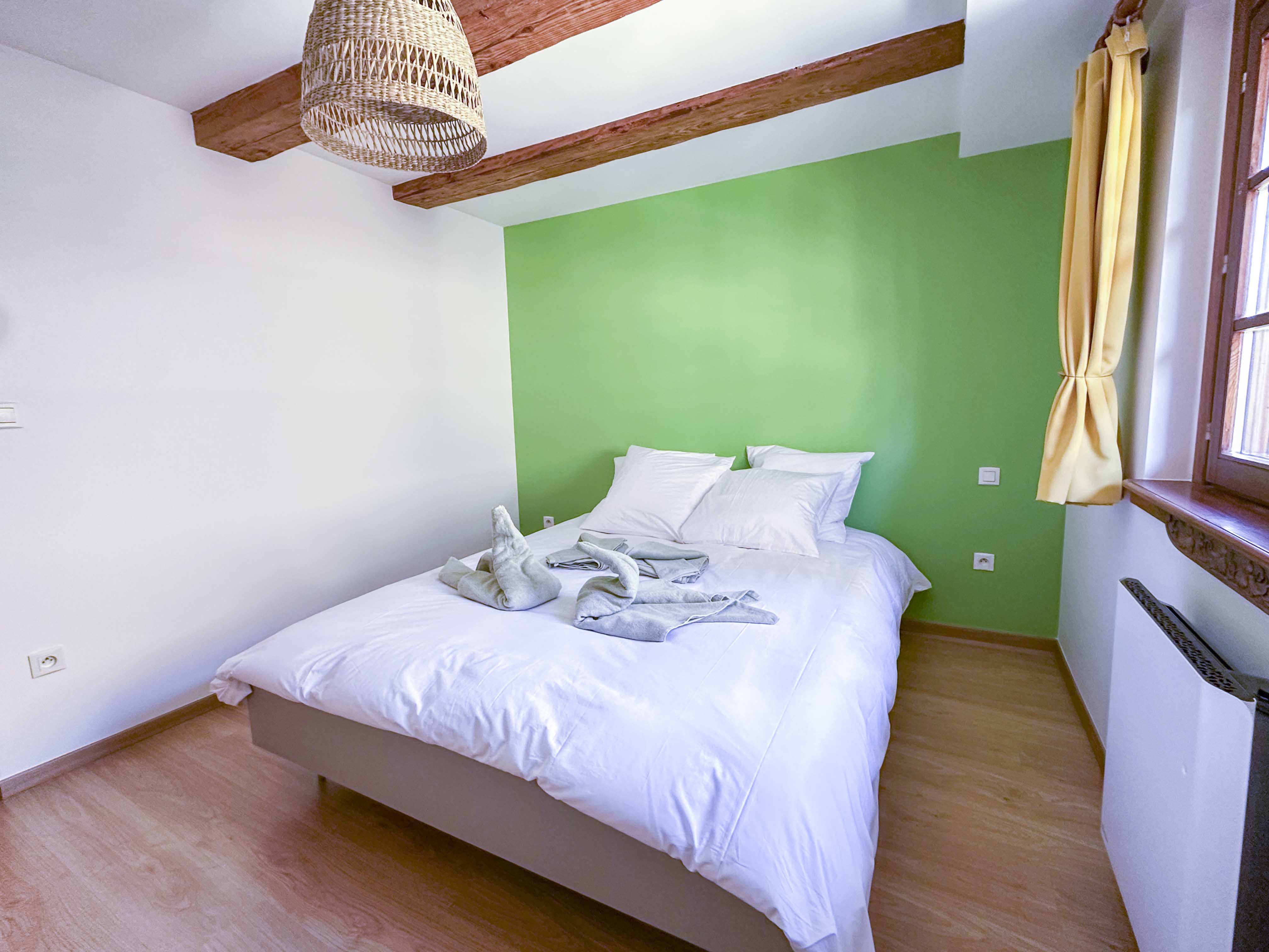 Chambre avec mur vert, poutres apparentes et lit double